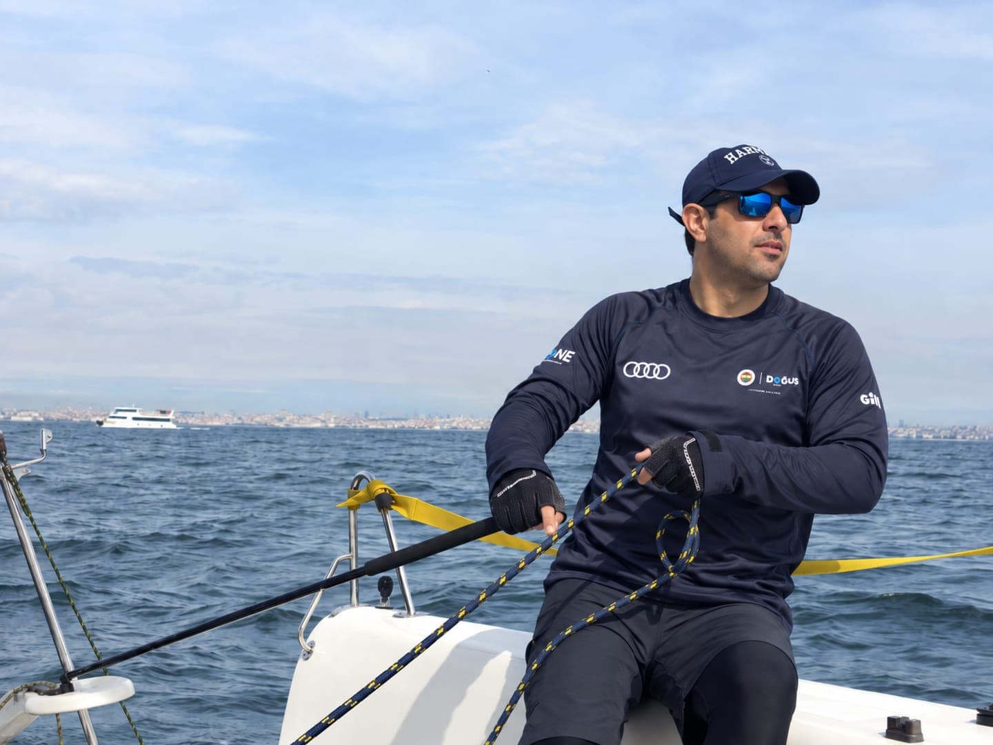 Buğra Bilim, Fenerbahçe Doğuş formasıyla teknede iskotayı tutarken; arkada İstanbul kıyısı.